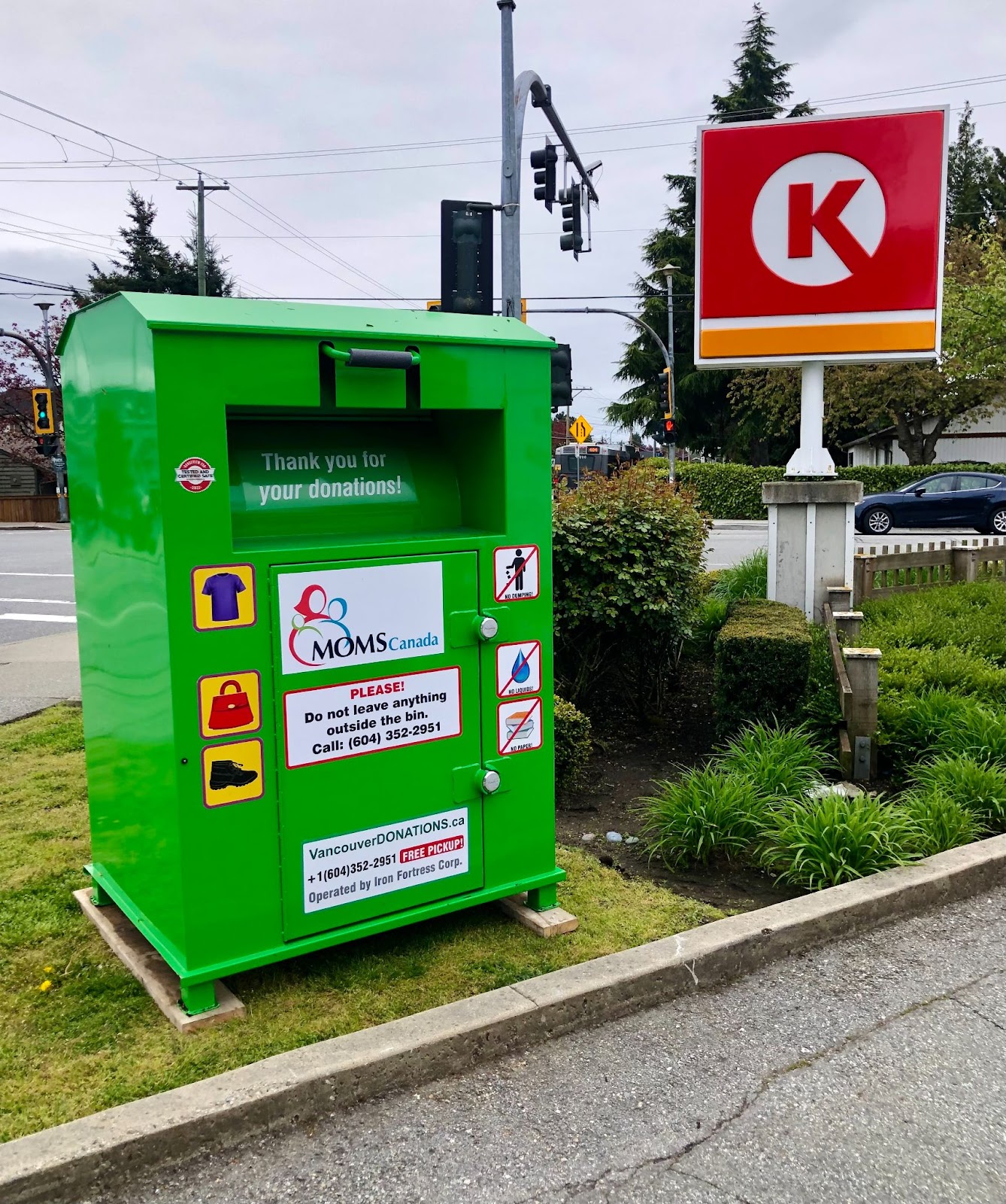 Green MOMS Canada donation bin for clothing and shoes with detailed instructions, located near a Circle K store in Vancouver.