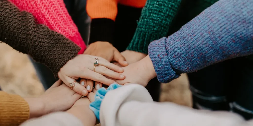 A group of individuals dressed in vibrant sweaters place their hands together in a huddle, embodying the essence of unity and teamwork with people_hands.