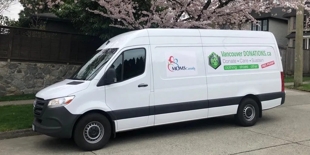 The vanpic shows a white delivery Eco-friendly donation parked on a residential street, featuring logos for Vancouver DONATIONS.ca and MOMS Canada on its side. In the background, there's a cherry blossom tree and a stone wall beside the street.